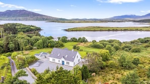 A house with a driveway, surrounded by lush greenery and a lake.