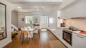Een moderne keuken met witte kasten, een ingebouwde oven en een eethoek met een witte tafel en stoelen.