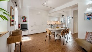 Een moderne keuken met witte kastjes, een eethoek met een ronde tafel en stoelen, en een zithoek met een bank.