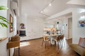 Eine moderne Küche mit weißen Schränken, ein Essbereich mit rundem Tisch und Stühlen sowie ein Wohnbereich mit einer Couch.