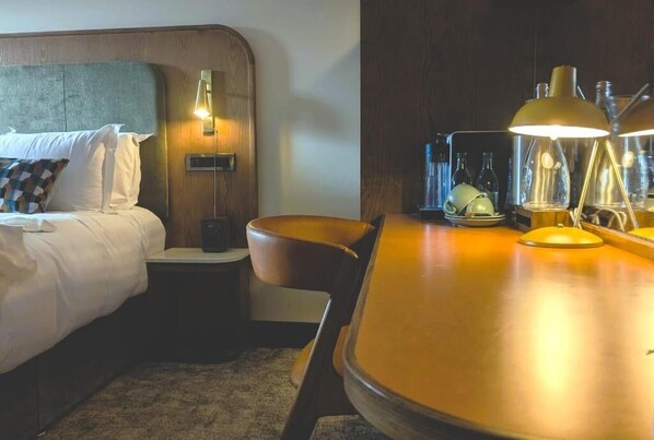 Una habitación de hotel con cama, mesita de noche, lámpara y una pequeña mesa con una silla.