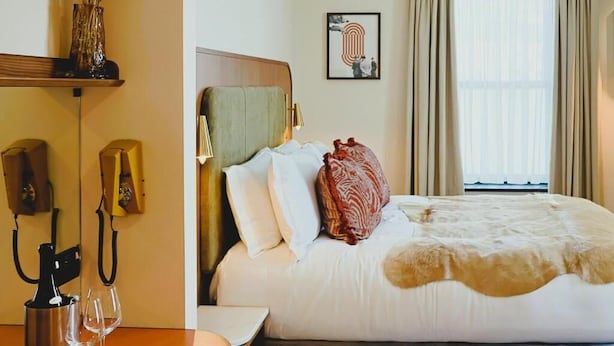 Una habitación de hotel con cama, mesita de noche, lámpara, teléfono y ventana con cortinas.