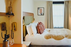 Una habitación de hotel con cama, mesita de noche, lámpara, teléfono y ventana con cortinas.