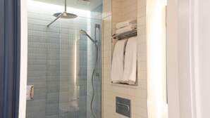 Ducha con mampara de vidrio, toallero con toallas dobladas y panel de control en la pared.
