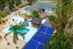 Une maison avec une piscine, un court de tennis et un patio aménagé avec des chaises et une petite terrasse.