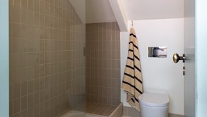 Ein Badezimmer mit Duschkabine aus Glas, einer weißen Toilette, einem Handtuchhalter mit einem gestreiften Handtuch und einem kleinen Teppich auf dem Boden.