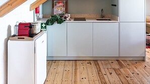Een compacte keuken met witte kasten, een magnetron en een spoelbak onder een schuine balkenplafond.
