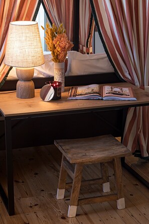 A cozy room with a wooden desk, a lamp, a vase with dried flowers, a candle, and a magazine. - The Old Net Studio in Porto Brandão (Caparica)