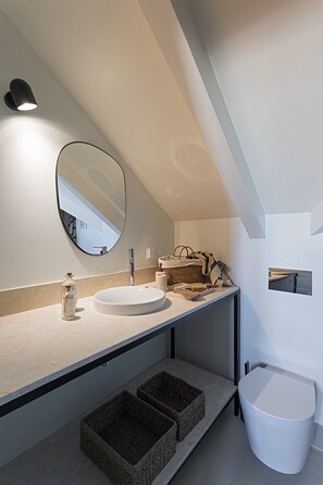 A modern bathroom with a round mirror, a sink, and a toilet. - The Old Net Studio in Porto Brandão (Caparica)