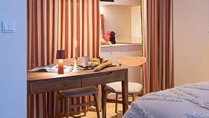 A compact hotel room with a bed, a desk with a chair, a microwave, and a small kitchenette. - Tanoeiro's Cottage in Porto Brandão (Caparica)