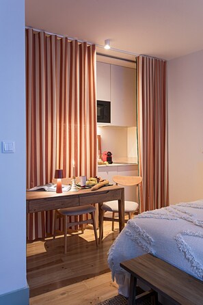 Ein kleines Hotelzimmer mit Bett, Schreibtisch mit Stuhl, Mikrowelle und einer kleinen Küchenzeile.