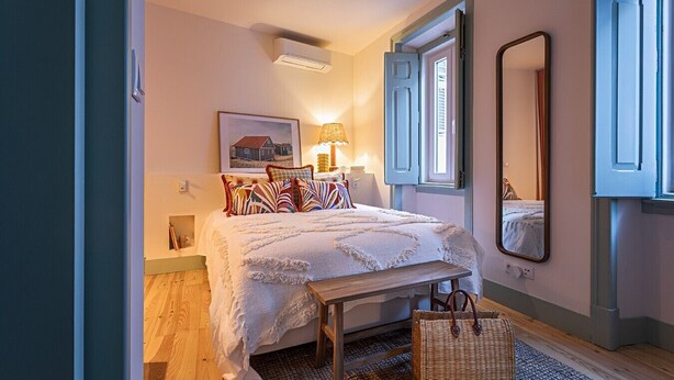 A bedroom with a bed, bedside table, lamp, window, and mirror. - Tanoeiro's Cottage in Porto Brandão (Caparica)