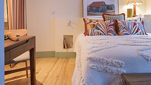 A bedroom with a bed, a wooden table, a lamp, and a framed picture on the wall. - Tanoeiro's Cottage in Porto Brandão (Caparica)