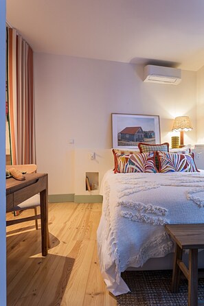 Ein Schlafzimmer mit einem Bett, einem Holztisch, einer Lampe und einem gerahmten Bild an der Wand.