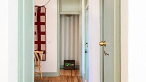 Um corredor com chão de madeira, parede listrada, uma cadeira e uma cômoda pequena.