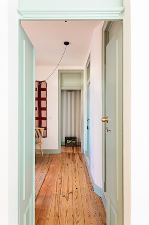 A hallway with wooden flooring, a striped wall, a chair, and a small chest of drawers. - Harbor Line Retreat in Porto Brandão (Caparica)
