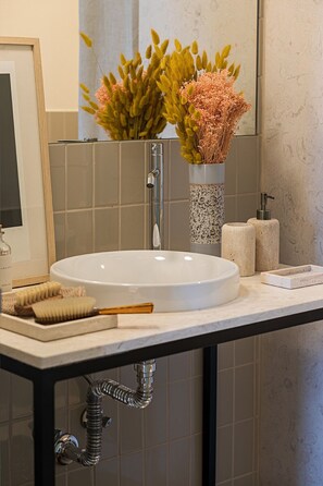A bathroom with a white sink, a mirror, a towel dispenser, and a vase with dried flowers. - Harbor Line Retreat in Porto Brandão (Caparica)