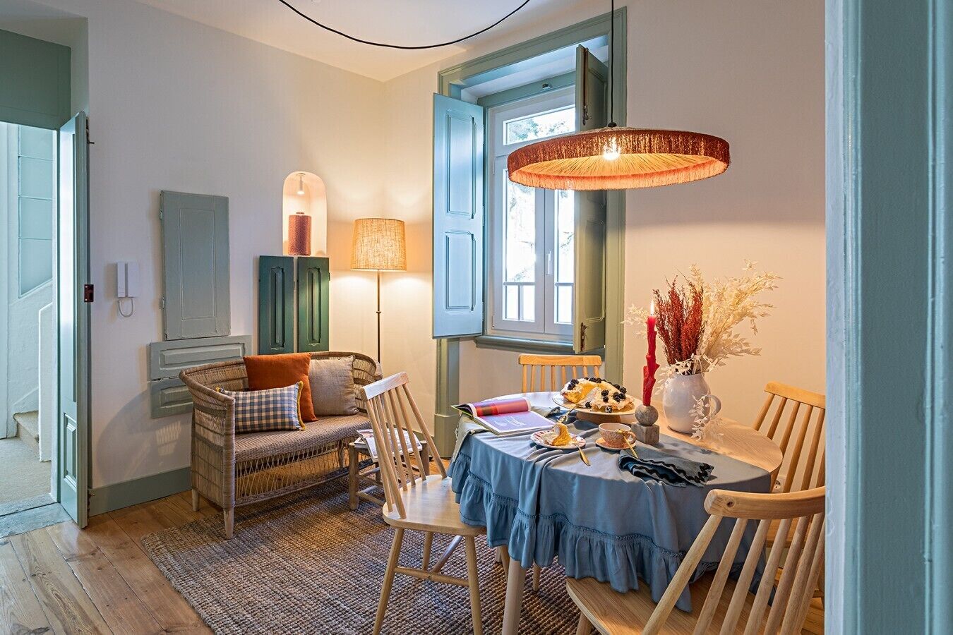 Uma área de refeições com mesa redonda, cadeiras, luminária e um vaso com flores secas.