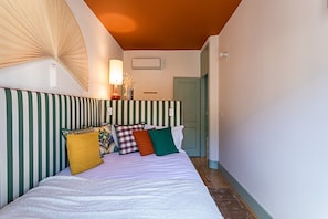 A bed with striped headboard, pillows, a bedside lamp, and a wall-mounted air conditioner. - Harbor Line Retreat in Porto Brandão (Caparica)
