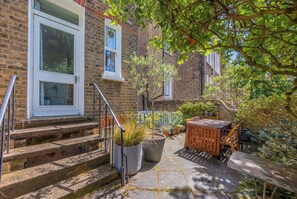 A brick building with a staircase leading to a door, potted plants, and outdoor furniture. - Chelsea Apartment | 2 Bedrooms | Spacious Garden (London)