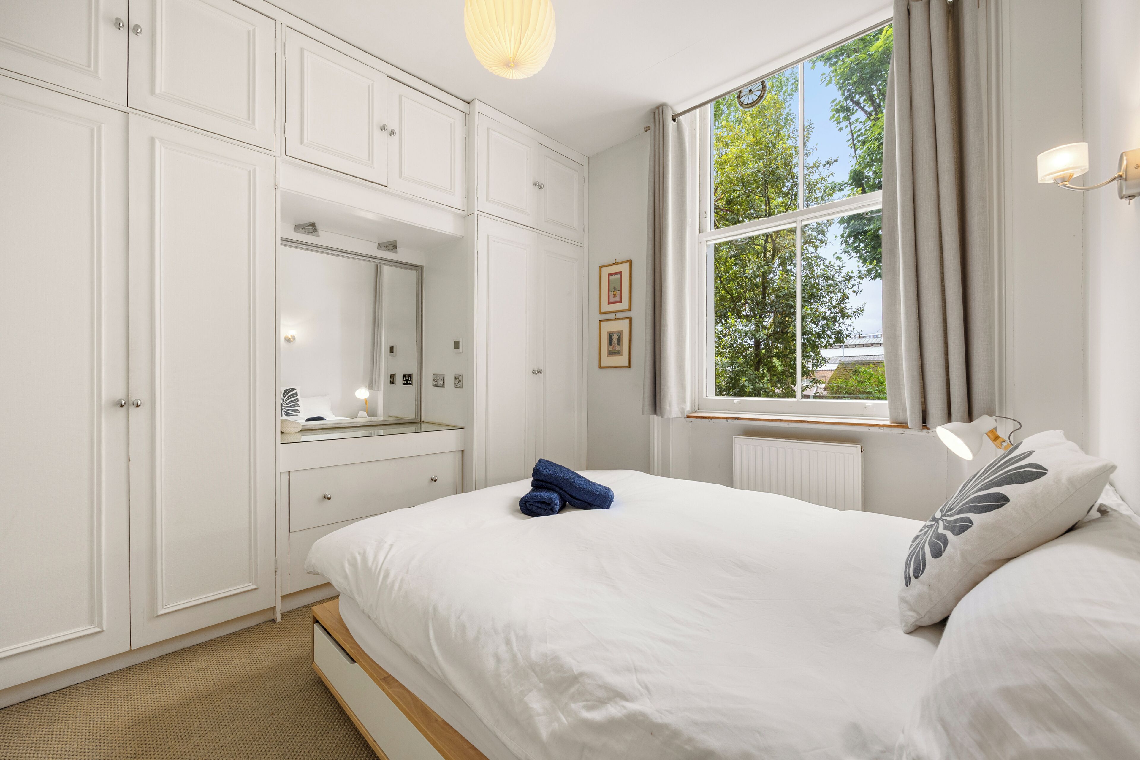 A bedroom with a bed, a dresser, a mirror, and a window with curtains.
