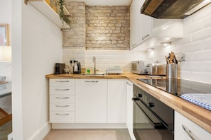 A compact kitchen with white cabinetry, a wooden countertop, a brick accent wall, and modern appliances. - Chelsea Apartment | 2 Bedrooms | Spacious Garden (London)