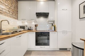 A modern kitchen with white cabinets, a Bosch oven, a microwave, and a brick wall backsplash. - Chelsea Apartment | 2 Bedrooms | Spacious Garden (London)