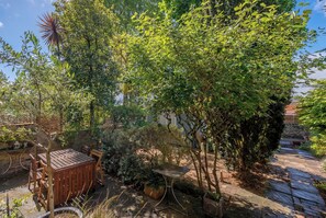 A patio with a wooden table and chairs, surrounded by lush greenery and a stone wall. - Chelsea Apartment | 2 Bedrooms | Spacious Garden (London)