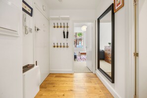 A hallway with wooden flooring, a coat rack, a telephone, and a mirror. - Chelsea Apartment | 2 Bedrooms | Spacious Garden (London)