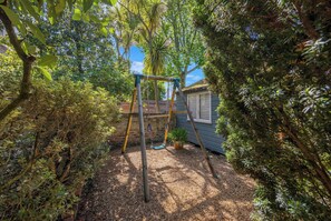A wooden swing set in a garden with dense foliage and a house in the background. - Chelsea Apartment | 2 Bedrooms | Spacious Garden (London)