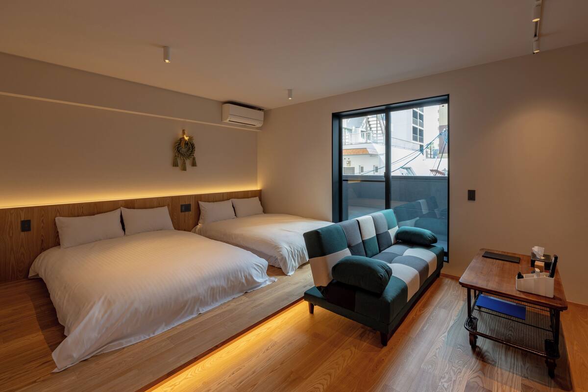 Una habitación de hotel moderna con dos camas, un sofá, una mesita y un ventanal con vistas a la ciudad.