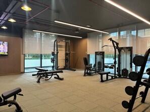Ein Fitnessraum mit Gewichthebern, Bänken und einem Fernsehbildschirm.