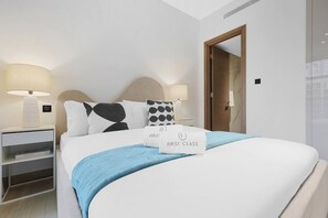 A hotel room with a bed, two bedside tables with lamps, a wooden door, and a mirror on the wall. - FIRST CLASS | 1BR | Contemporary Meydan Living (Meydan)