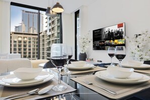 A dining table set with plates, bowls, wine glasses, and cutlery, with a cityscape view through large windows. - FIRST CLASS | 1BR | Contemporary Meydan Living (Meydan)