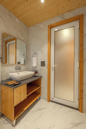 Un baño con tocador de madera, un lavabo blanco, un espejo y una puerta de vidrio esmerilado.