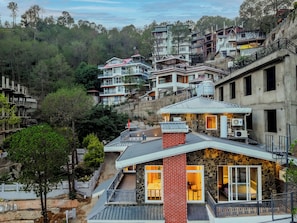 A hillside residential area with modern houses, some with balconies and large windows. - ELIVAAS Bask and Blessings Meadows 3BHK (Anhech)