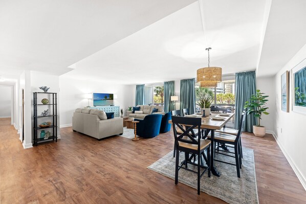 A spacious living area with a dining table, sofas, and a large window with curtains. - $150 Free activities - E-gift card when you book- On the ocean | SH105 (Myrtle Beach)