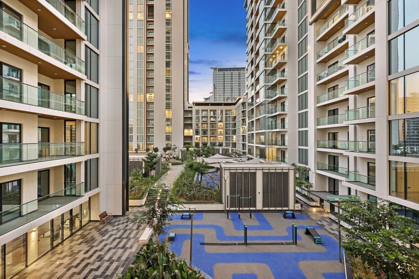A modern high-rise building with multiple balconies, a central courtyard with a pool, and surrounding greenery.
