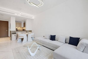 A modern living room with a sofa, a glass coffee table, and a dining area with chairs and a table. - FIRST CLASS | 1BR | Chic Glimpse Near Downtown (Meydan)