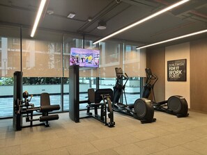 A gym with exercise equipment, a television, and a motivational poster. - FIRST CLASS | 1BR | Chic Glimpse Near Downtown (Meydan)