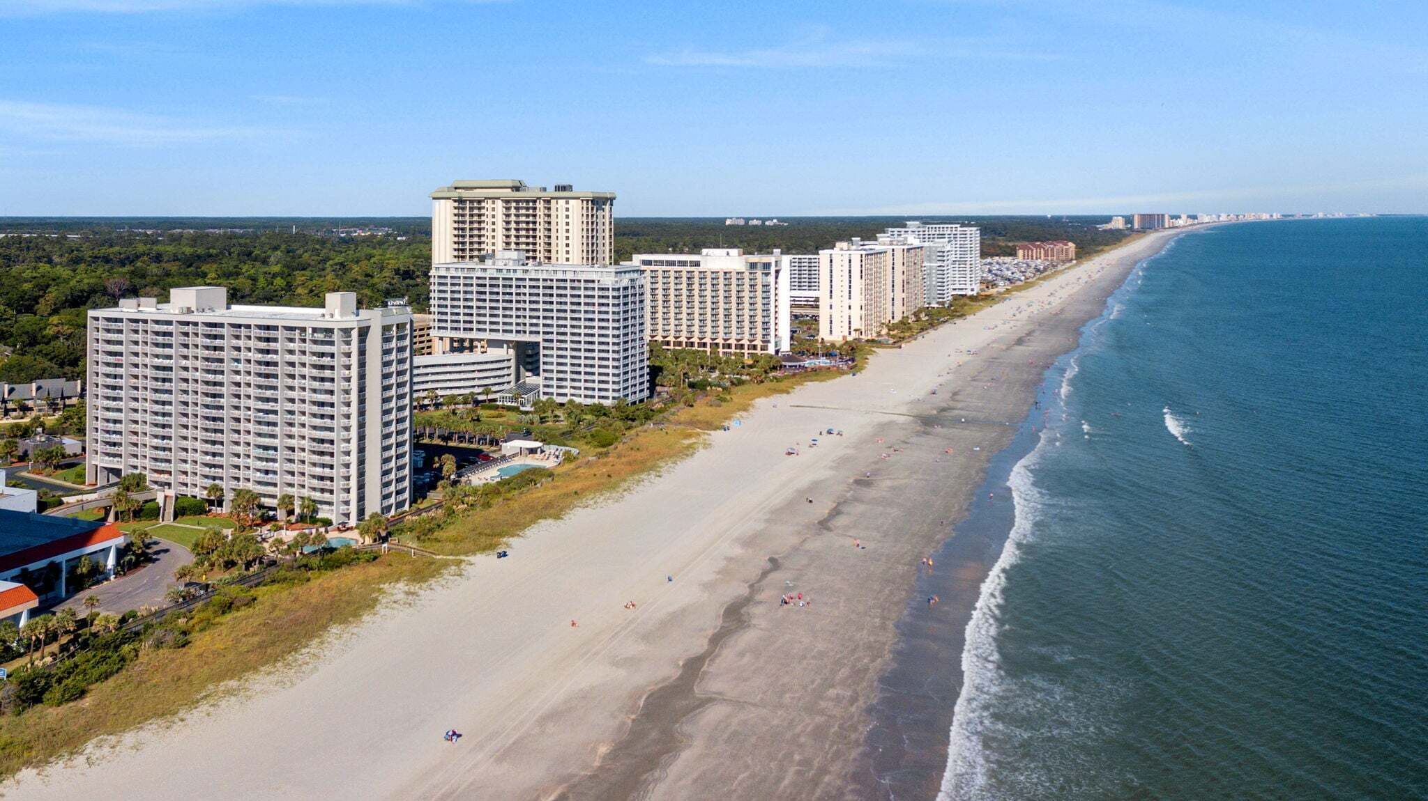 A coastal cityscape with high-rise hotels, a sandy beach, and a clear view of the ocean.