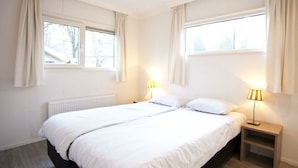Ett sovrum med en stor säng, två sänglampor, ett fönster och ett element.