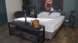A bedroom with a bed, a desk with a computer, a lamp, and a painting on the wall. - Comfort Room Deluxe 2 (Otterlo)