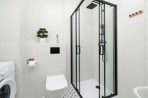 Et moderne badeværelse med en brusekabine med glasvægge, toilet, vaskemaskine og en lille potteplante.