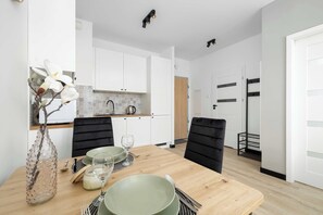 Een moderne keuken met witte kasten, een betegelde spatwand en een eethoek met een houten tafel en zwarte stoelen.