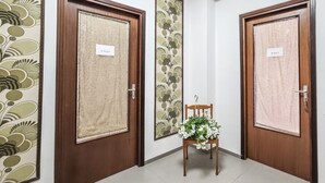 Ein Flur mit zwei Holztüren, auf denen 'Il Vico 1' und 'Il Vico 2' steht, einem kleinen Holzstuhl und einer Blumendekoration, sowie einem Wandteppich mit Muster an der linken Wand.