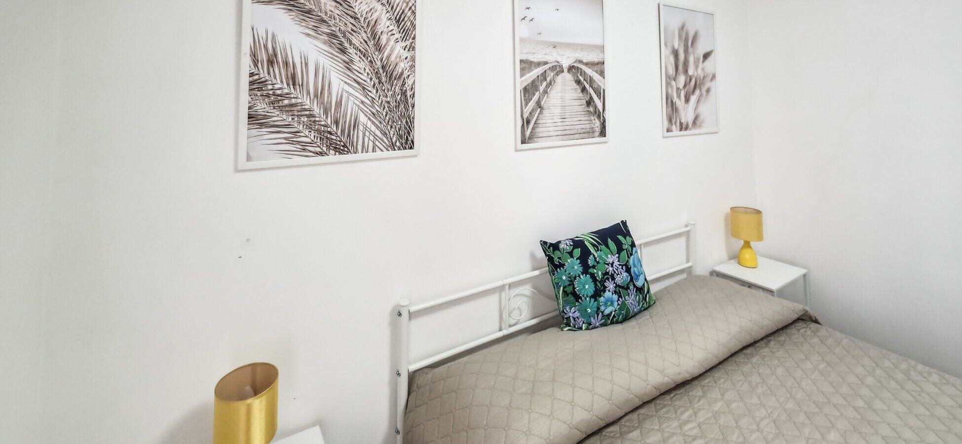 A bedroom with a bed, a nightstand, a lamp, and three framed pictures on the wall.