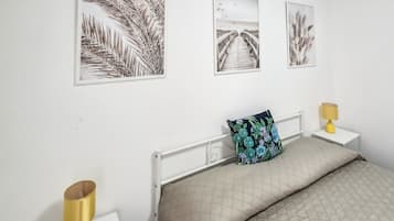 A bedroom with a bed, a nightstand, a lamp, and three framed pictures on the wall.