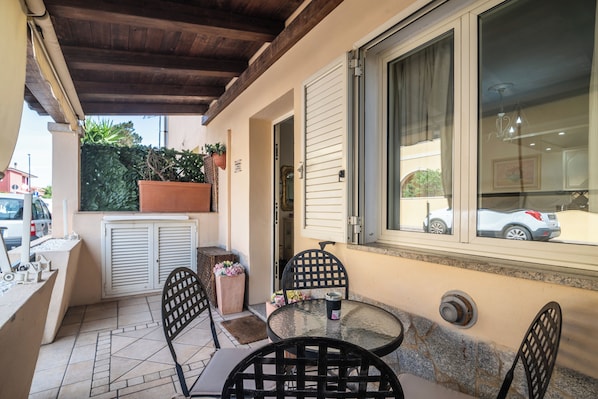 An outdoor patio with a round table, two chairs, a potted plant, and a window with a view of a car. - San Nikola House (Olbia)