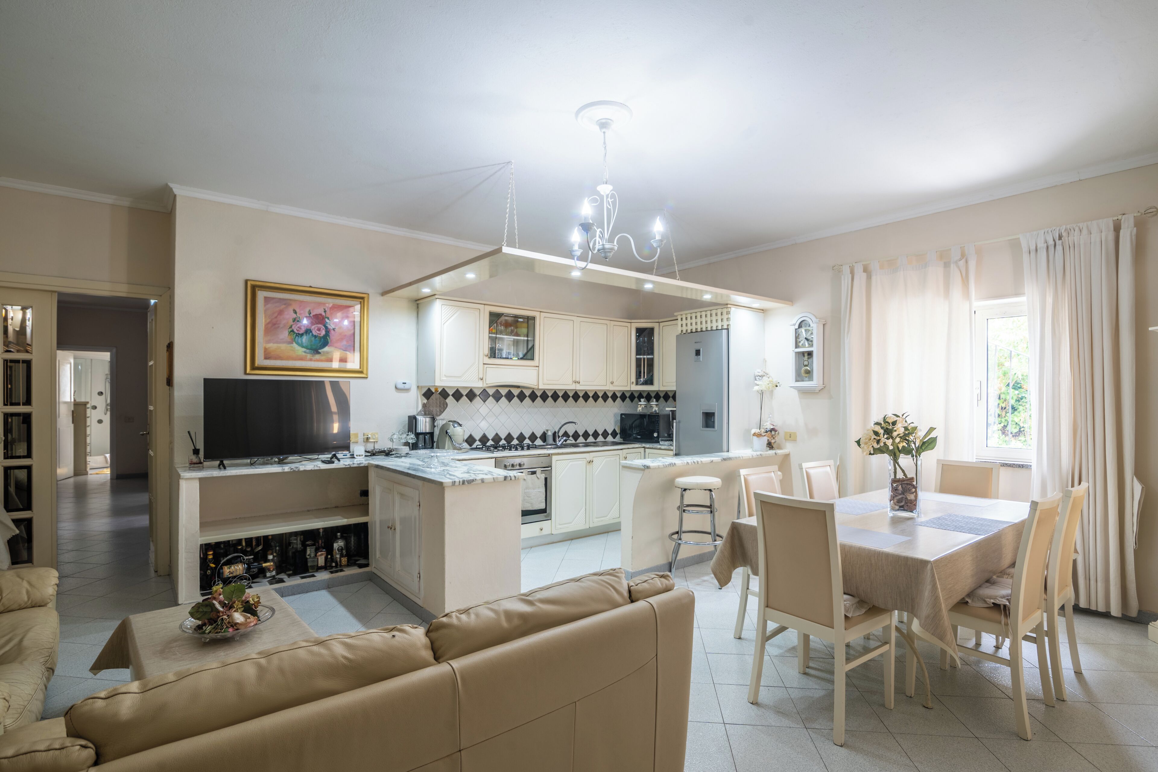 Un salon moderne comprenant un canapé, une table à manger avec des chaises, un coin cuisine avec un téléviseur et un lustre.